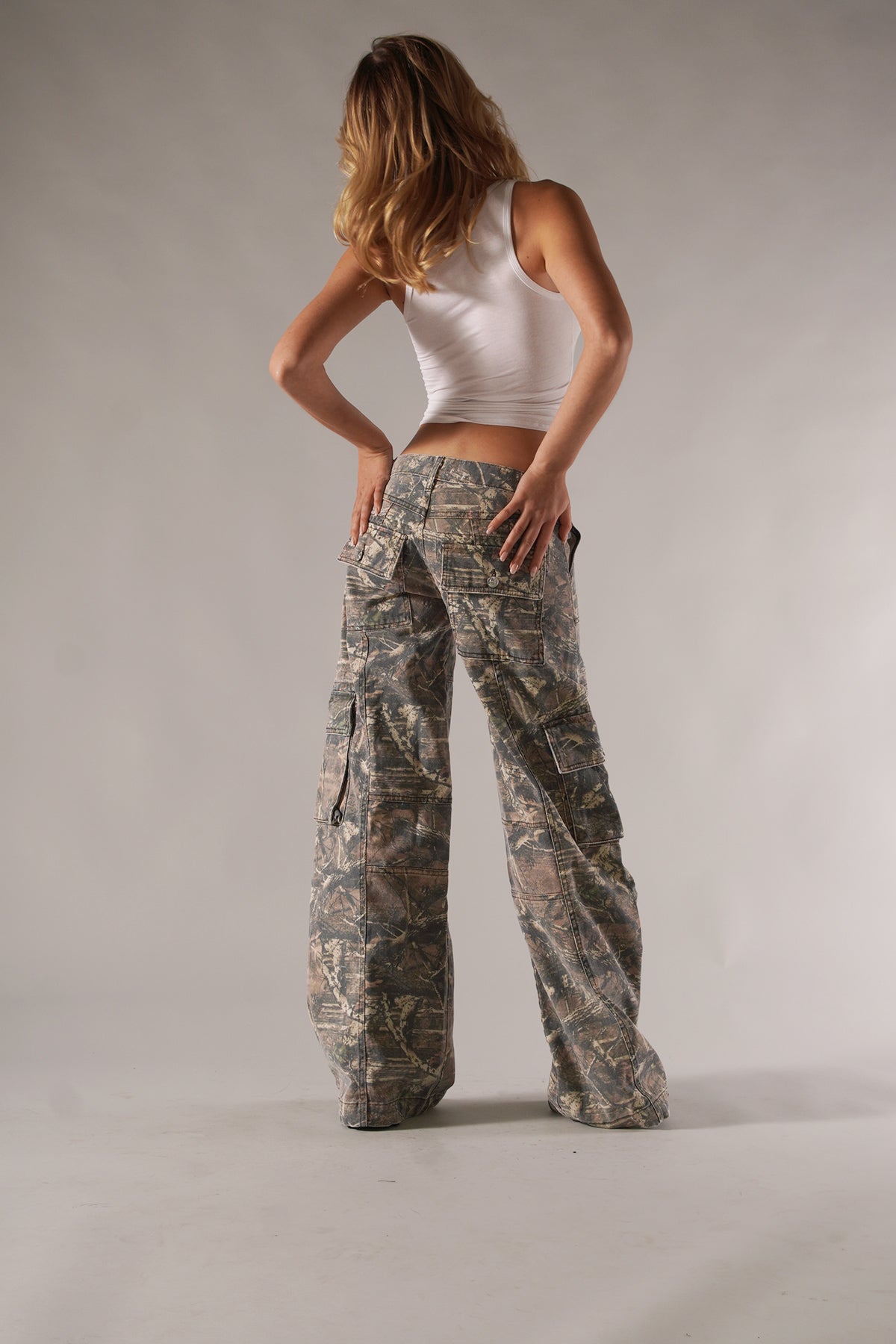 Frau in weißem Tanktop und Camouflage-Cargohose, Mode, Freizeitkleidung, Rückansicht.