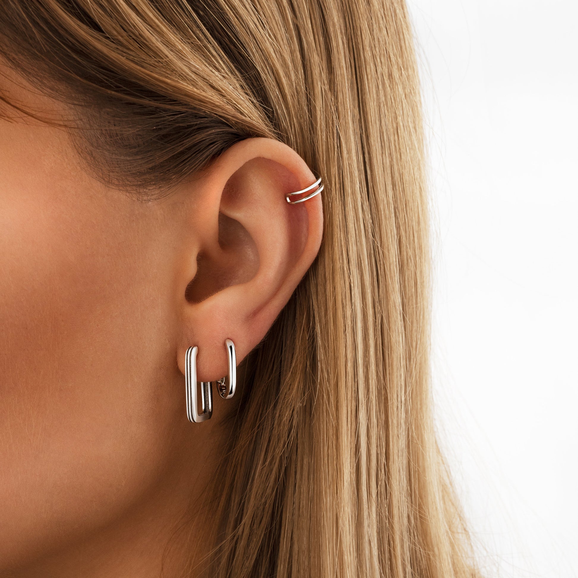 Frau mit silbernen Creolen und Ohrklemme, Nahaufnahme, modischer Ohrschmuck, minimalistisches Design.