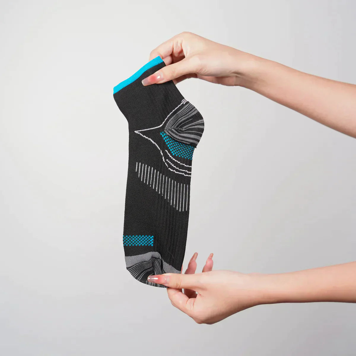Schwarze Sportsocke mit blau-grauem Muster, in Händen gehalten, auf weißem Hintergrund.