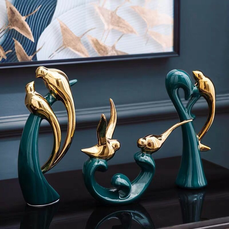 Goldene und grüne Vogelskulpturen aus Keramik auf schwarzem Tisch, moderne Wohnkultur.