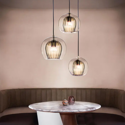 Drei moderne Glas-Pendelleuchten über rundem Marmortisch in elegantem Esszimmer.