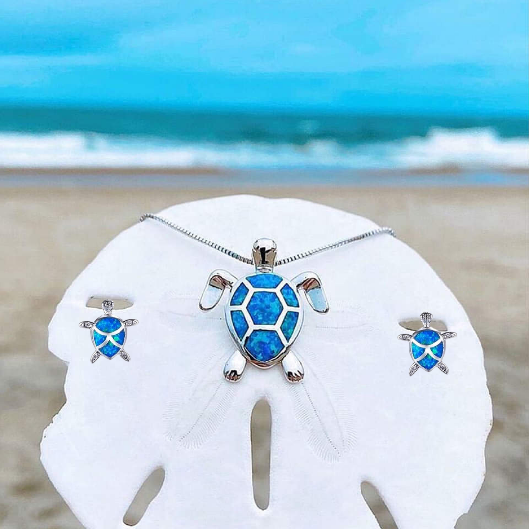 Silberne Schildkröten-Halskette und Ohrringe mit blauem Opal am Strand vor dem Meer.