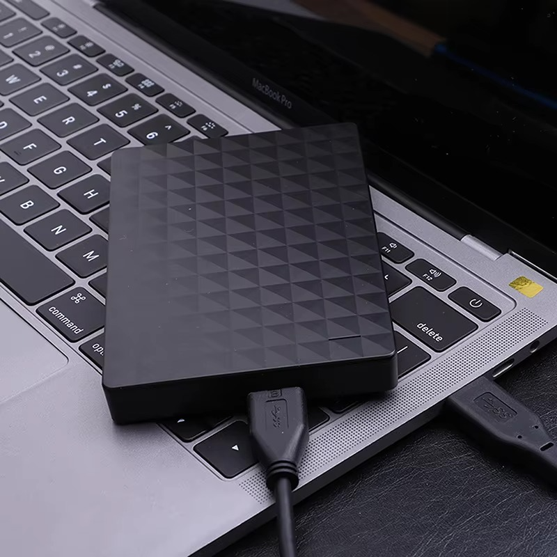 Hårddisken ligger på tangentbordet till en bärbar dator och är ansluten med en svart USB-kabel 3