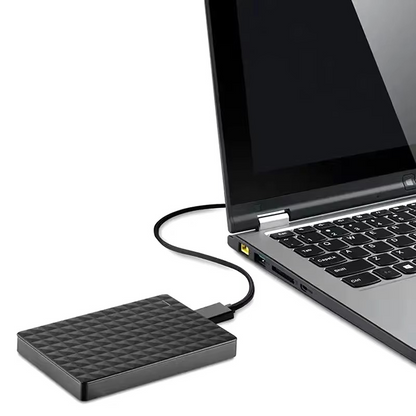 Hårddisken står på bordet bredvid en öppen bärbar dator och är kopplad med en kabel till dess USB-port 5