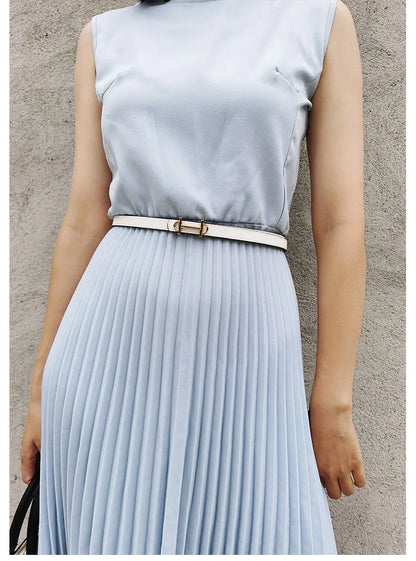Frau in hellblauem Kleid mit weißem Gürtel und H-Schnalle vor grauer Wand.