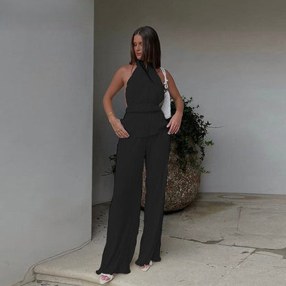 Frau in schwarzem ärmellosen Jumpsuit, elegante Mode, Sommeroutfit, vor modernem Gebäude.