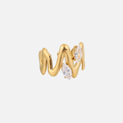 Sidovy av den guldfärgade ringen med vågformad, skulptural design och två klara avlånga stenar i infattning. 2