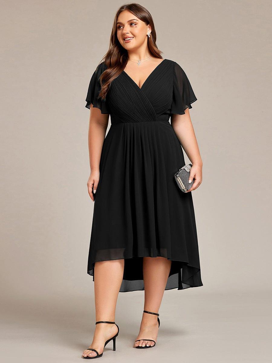 Svart klänning på plus size-modell i helfigur framifrån, hållande en liten glittrande clutch och med svarta klackar. 30