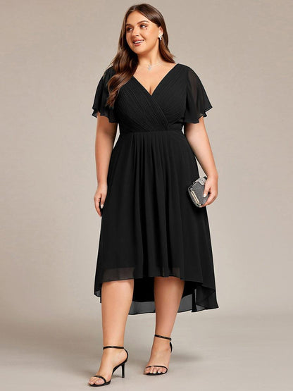 Svart klänning på plus size-modell i helfigur framifrån, hållande en liten glittrande clutch och med svarta klackar. 30