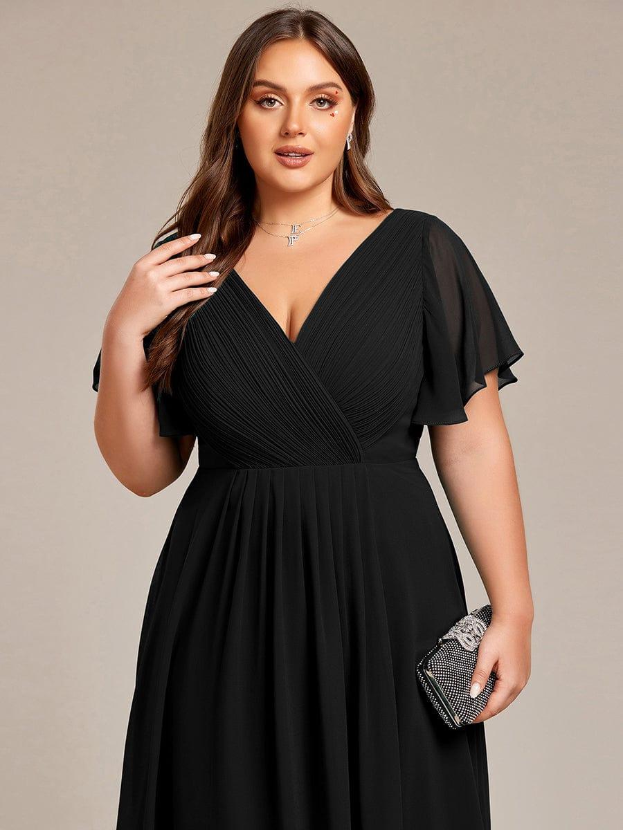 Närbild på överdelen av svart klänning på plus size-modell med veckat omlott-liv, skira ärmar och en glittrande clutch. 28