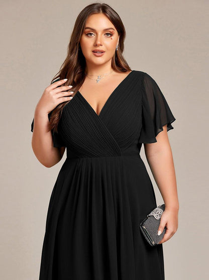 Närbild på överdelen av svart klänning på plus size-modell med veckat omlott-liv, skira ärmar och en glittrande clutch. 28