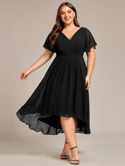 Svart klänning på plus size-modell som sträcker ut ena armen så att den flödande, asymmetriska kjolen syns, framifrån. 26