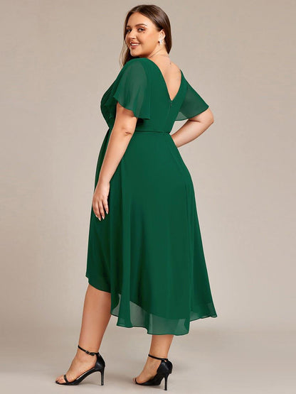 Mörkgrön klänning på plus size-modell bakifrån med V-ringad rygg, dragkedja och skira vingärmar, hon ser över axeln. 37