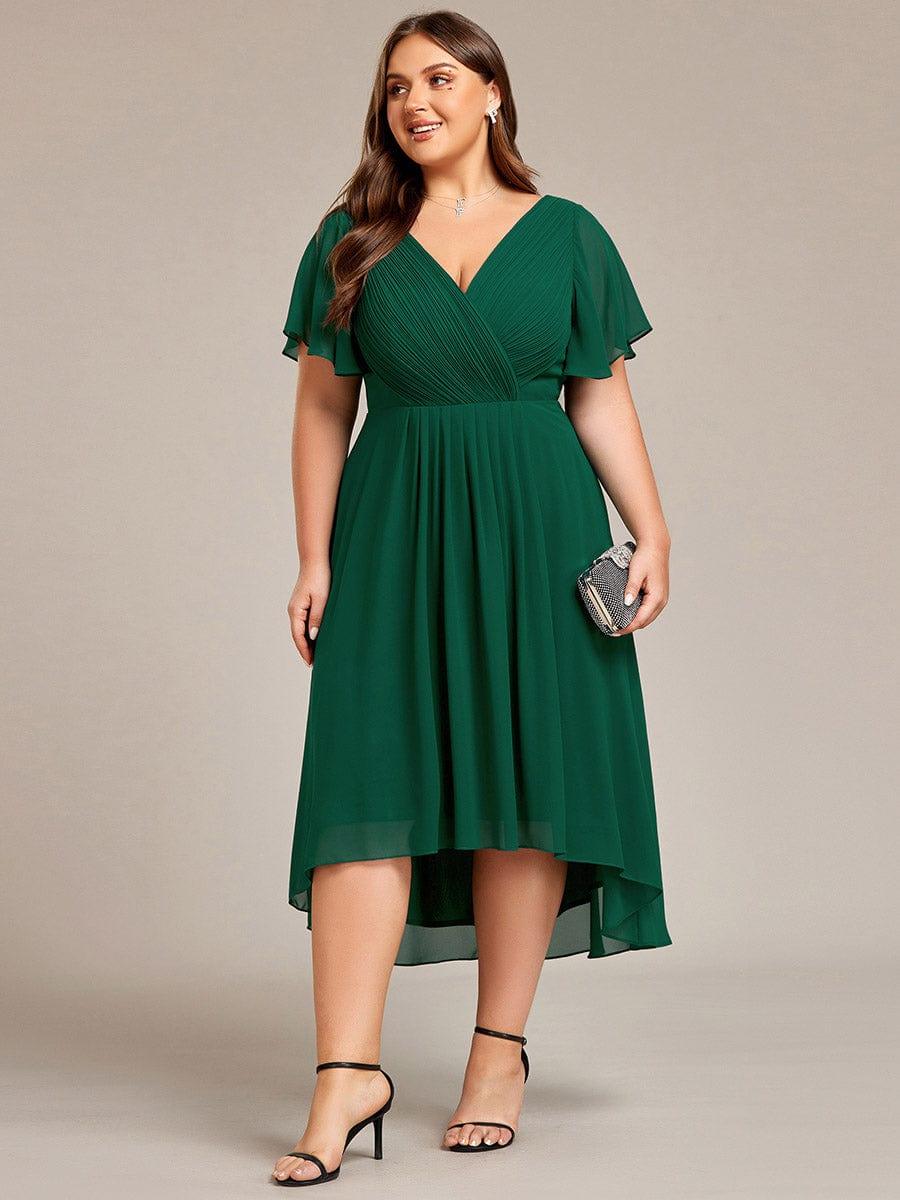 Mörkgrön klänning på plus size-modell i helfigur framifrån, med en liten glittrande clutch i handen och svarta klackar. 40