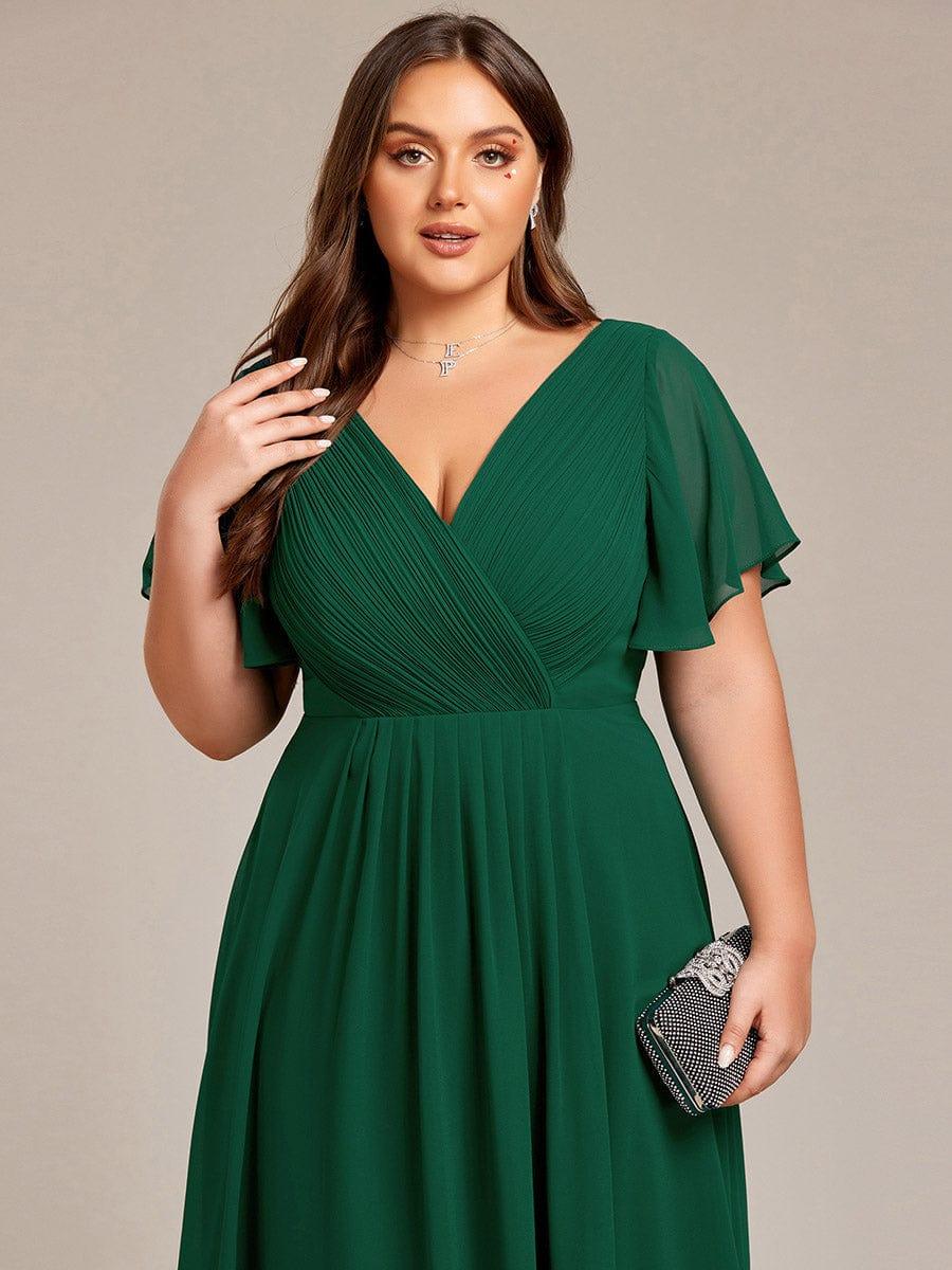 Närbild på överdelen av mörkgrön klänning med veckat omlott-liv och skira ärmar, modellen håller en glittrande clutch. 38