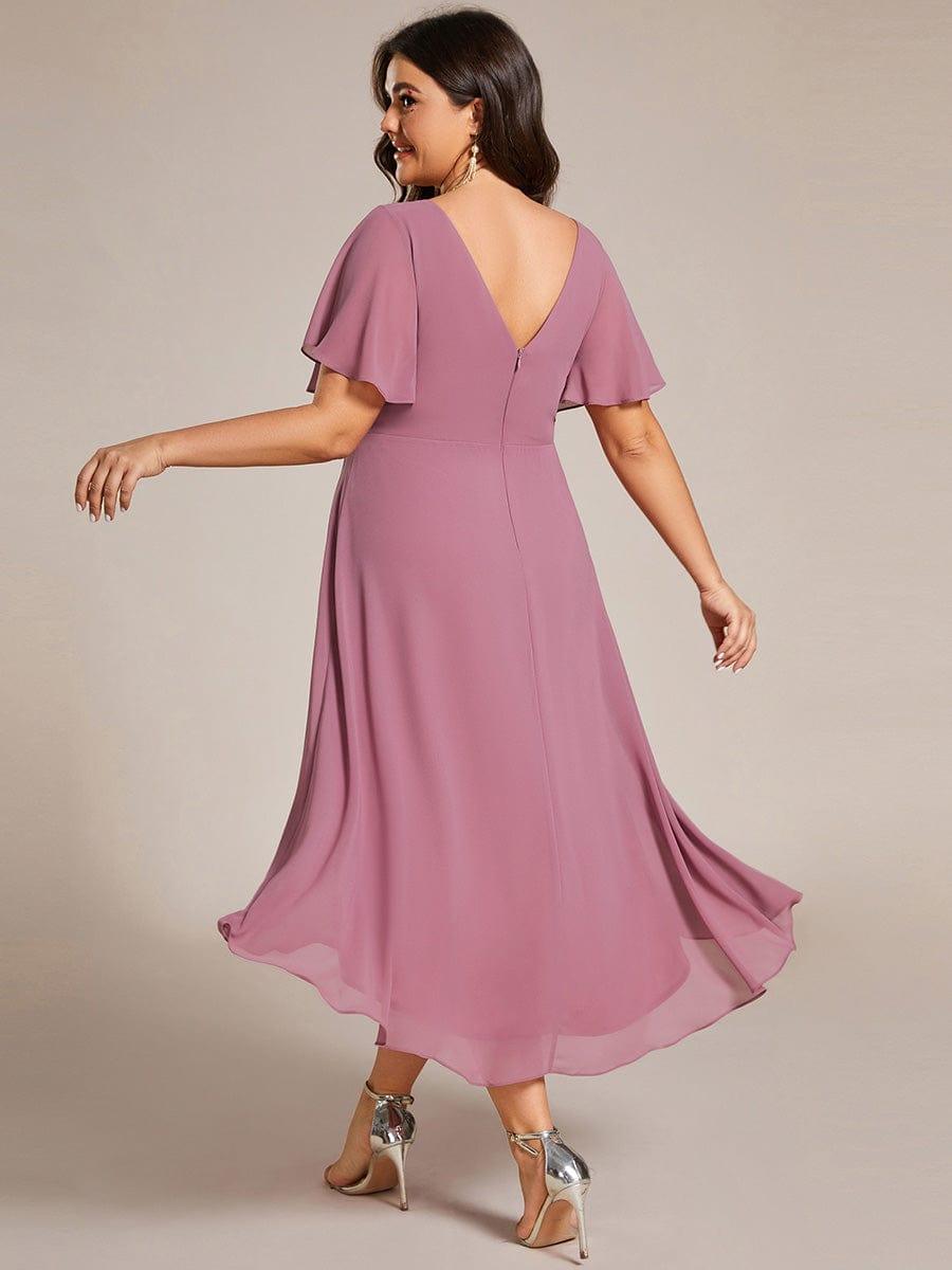 Plus size-modell i dammrosa klänning sedd bakifrån, med djup V-ringad rygg, dragkedja och lång, flödande bakkant. 64