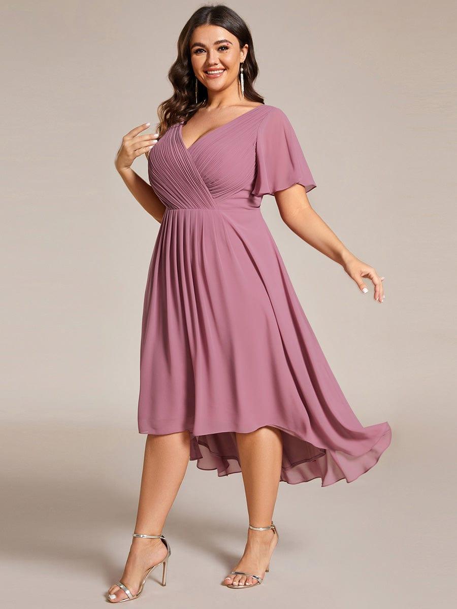 Plus size-modell i rörelse i dammrosa klänning, snett framifrån, med fladdrande kjol som är längre bak. 67