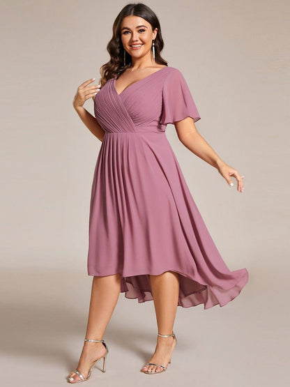 Plus size-modell i rörelse i dammrosa klänning, snett framifrån, med fladdrande kjol som är längre bak. 67