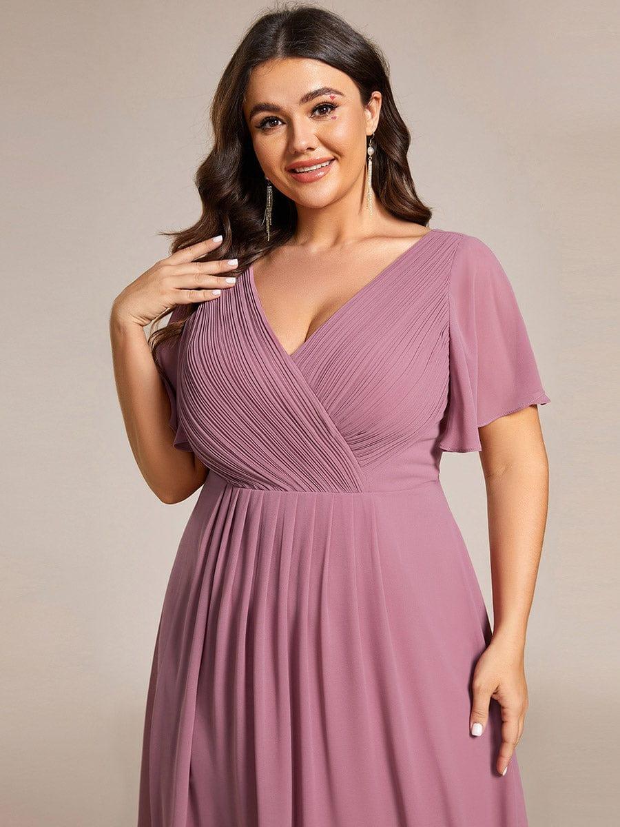 Närbild av plus size-modell i dammrosa klänning med veckad omlottöverdel, V-ringning och vida ärmar. 65