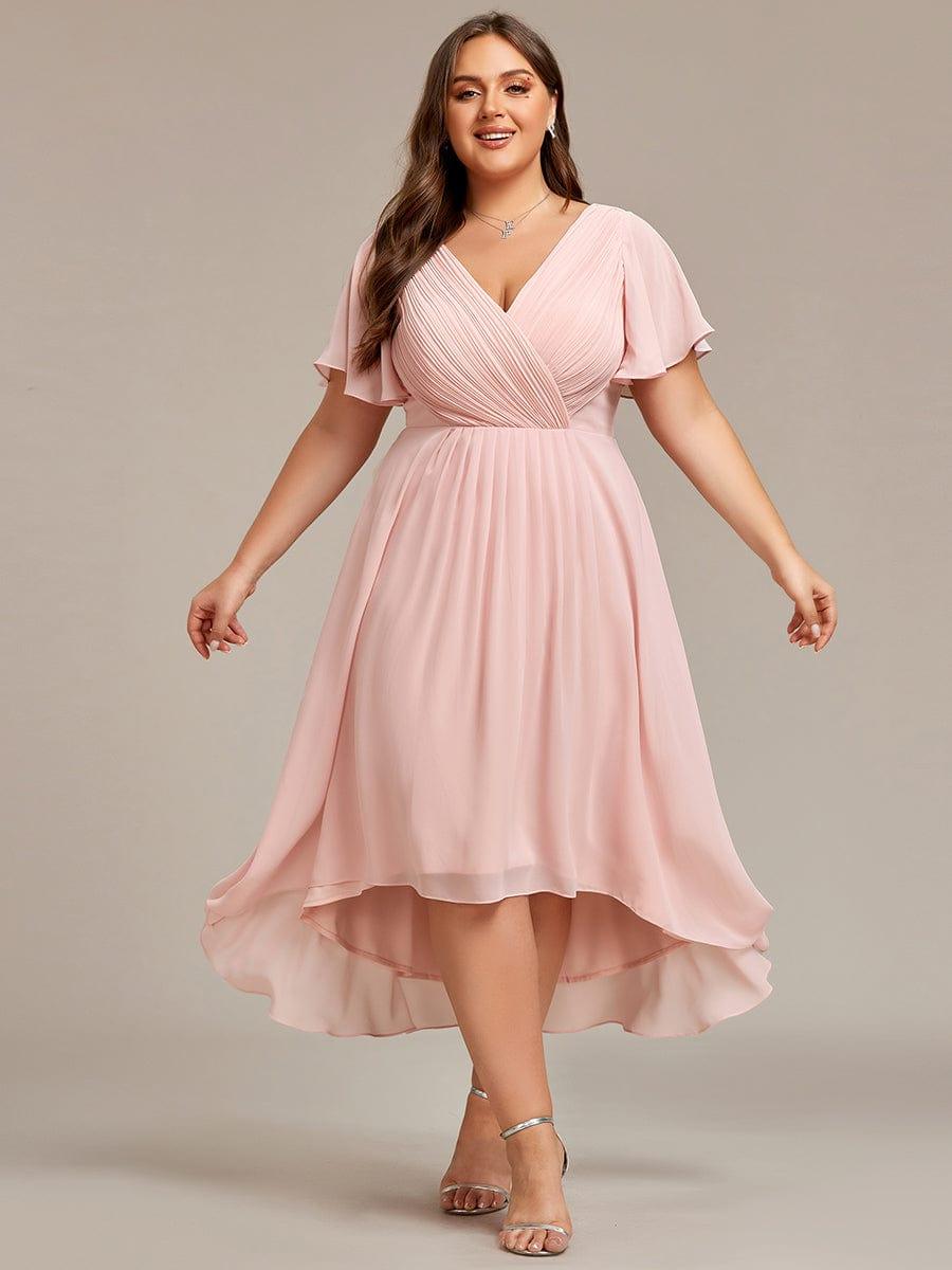 Ljusrosa klänning på plus size-modell i helfigur framifrån med armarna lätt utsträckta och silverfärgade sandaletter. 35