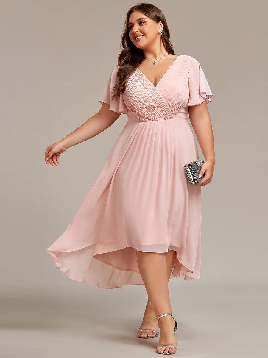 Ljusrosa klänning på plus size-modell som tittar åt sidan med en glittrande clutch i handen, snett framifrån. 31