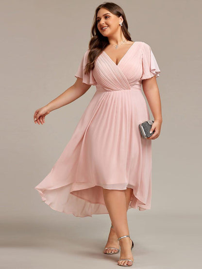 Ljusrosa klänning på plus size-modell som tittar åt sidan med en glittrande clutch i handen, snett framifrån. 31