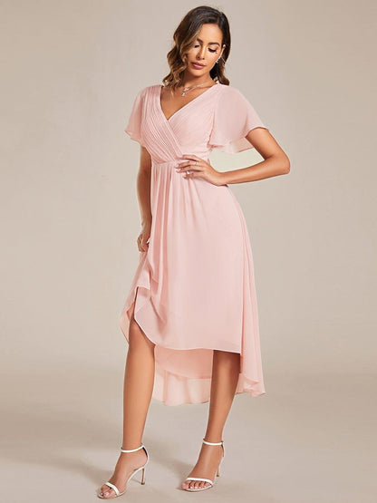 Rosa klänning där modellen lyfter fållen med ena handen och visar den lägre bak och högre fram, med vita sandaletter. 19