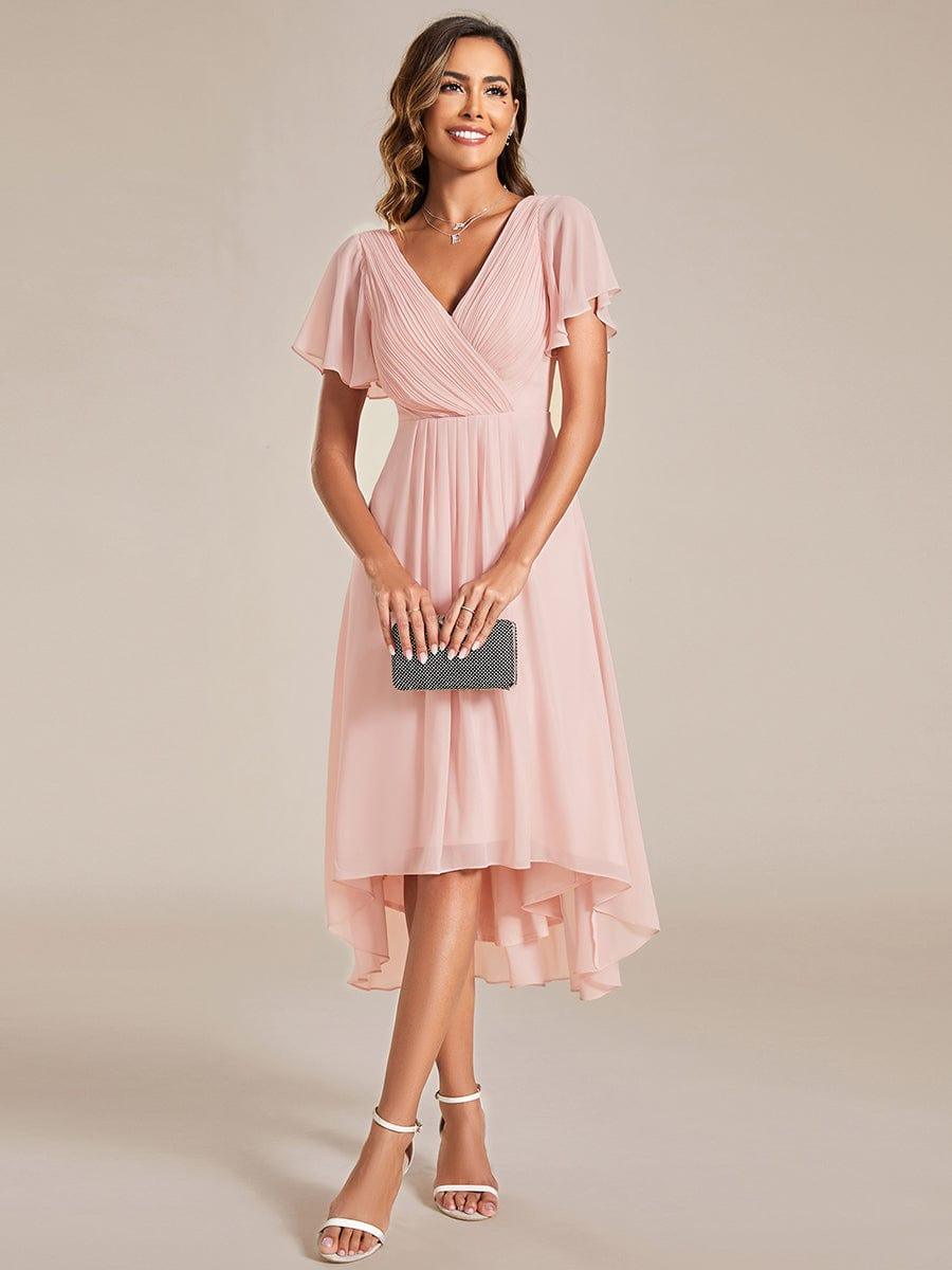 Rosa klänning med draperad V-ringning och fladdrande ärmar, modellen håller en svart glittrig clutch framför sig. 15