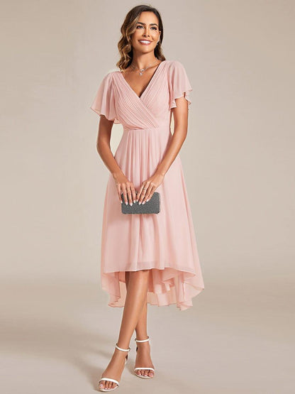 Rosa klänning med draperad V-ringning och fladdrande ärmar, modellen håller en svart glittrig clutch framför sig. 15