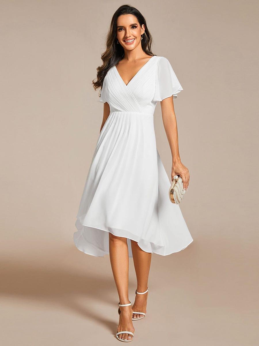 Modell i vit chiffongklänning med V-ringning och korta ärmar, framifrån, med vita sandaletter och en pärlbesatt clutch. 68