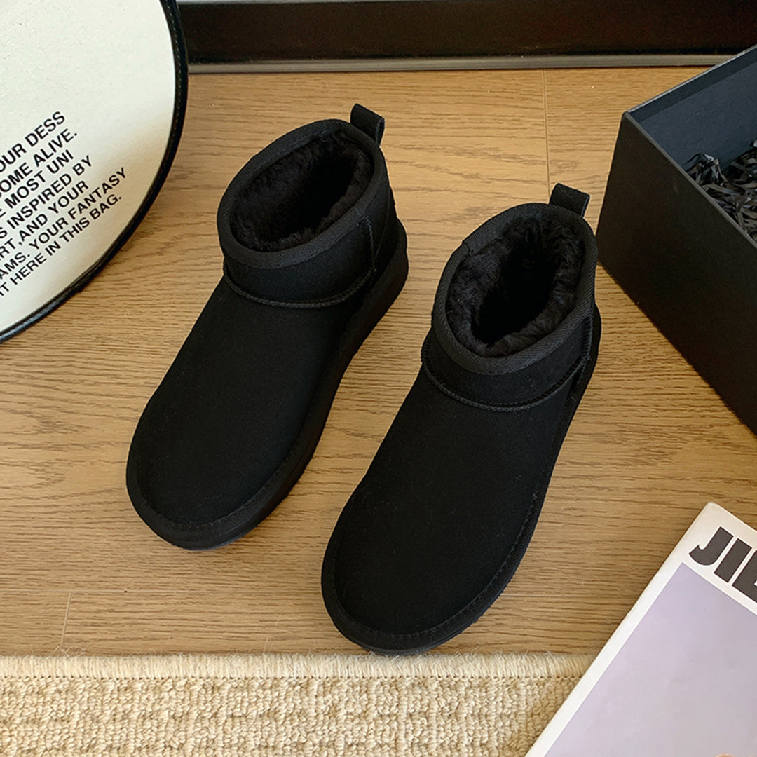 Schwarze Winterstiefel aus Wildleder mit Fellfutter auf Holzboden neben Karton.