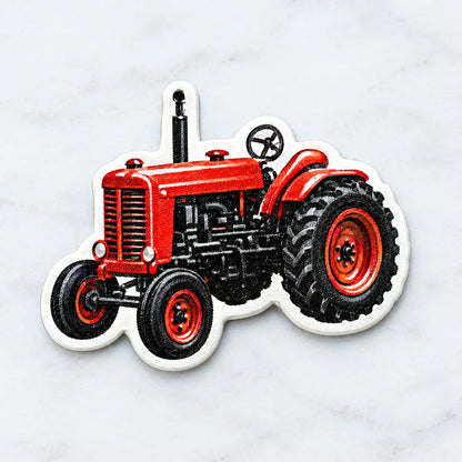 Närbild på en röd traktor i form av en dekoration med hål upptill för upphängning, liggande på en ljus marmoryta. 3