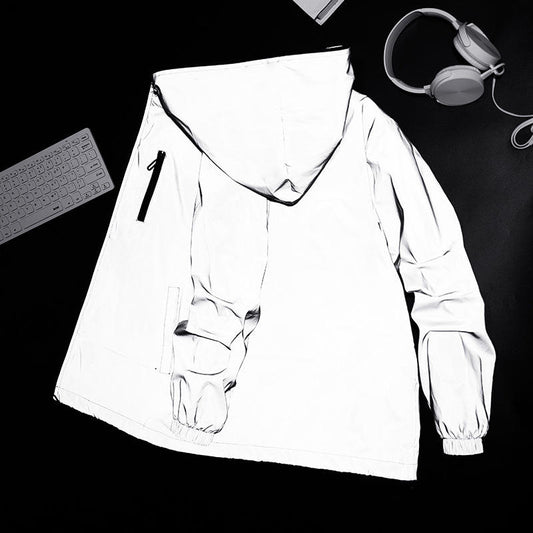 Weiße reflektierende Jacke mit Kapuze auf schwarzem Hintergrund, neben Tastatur und Kopfhörer.