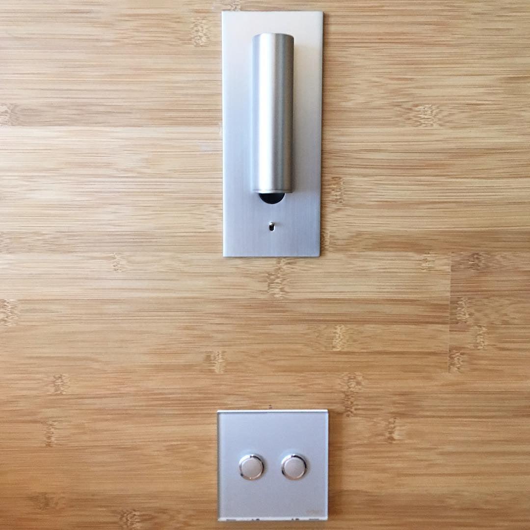 Silverfärgad vägglampa med nedfälld cylinder på träpanel ovanför en tvåknappsbrytare 34
