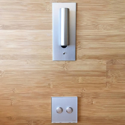 Silverfärgad vägglampa med nedfälld cylinder på träpanel ovanför en tvåknappsbrytare 34