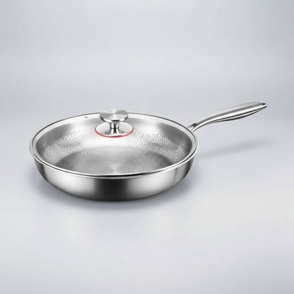 Stekpannan med glaslock och metallknopp, fotograferad snett från sidan mot ljusgrå bakgrund, med långt skaft i metall. 8
