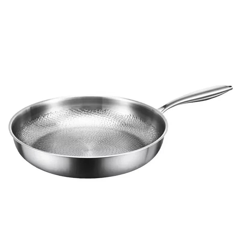 Stekpanna i blankt silverfärgat metall med hamrat mönster på insidan och långt skaft, fotograferad snett uppifrån mot vit bakgrund. 1