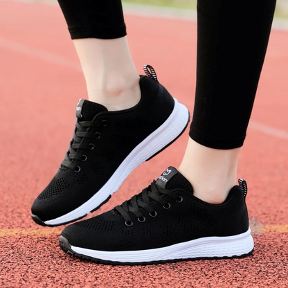 Schwarze Damen-Sneaker, atmungsaktiv, leicht, mit weißer Sohle, auf Laufbahn.