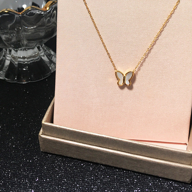 Goldene Schmetterlingskette auf rosa Hintergrund, modisch, elegant, Damenaccessoire.