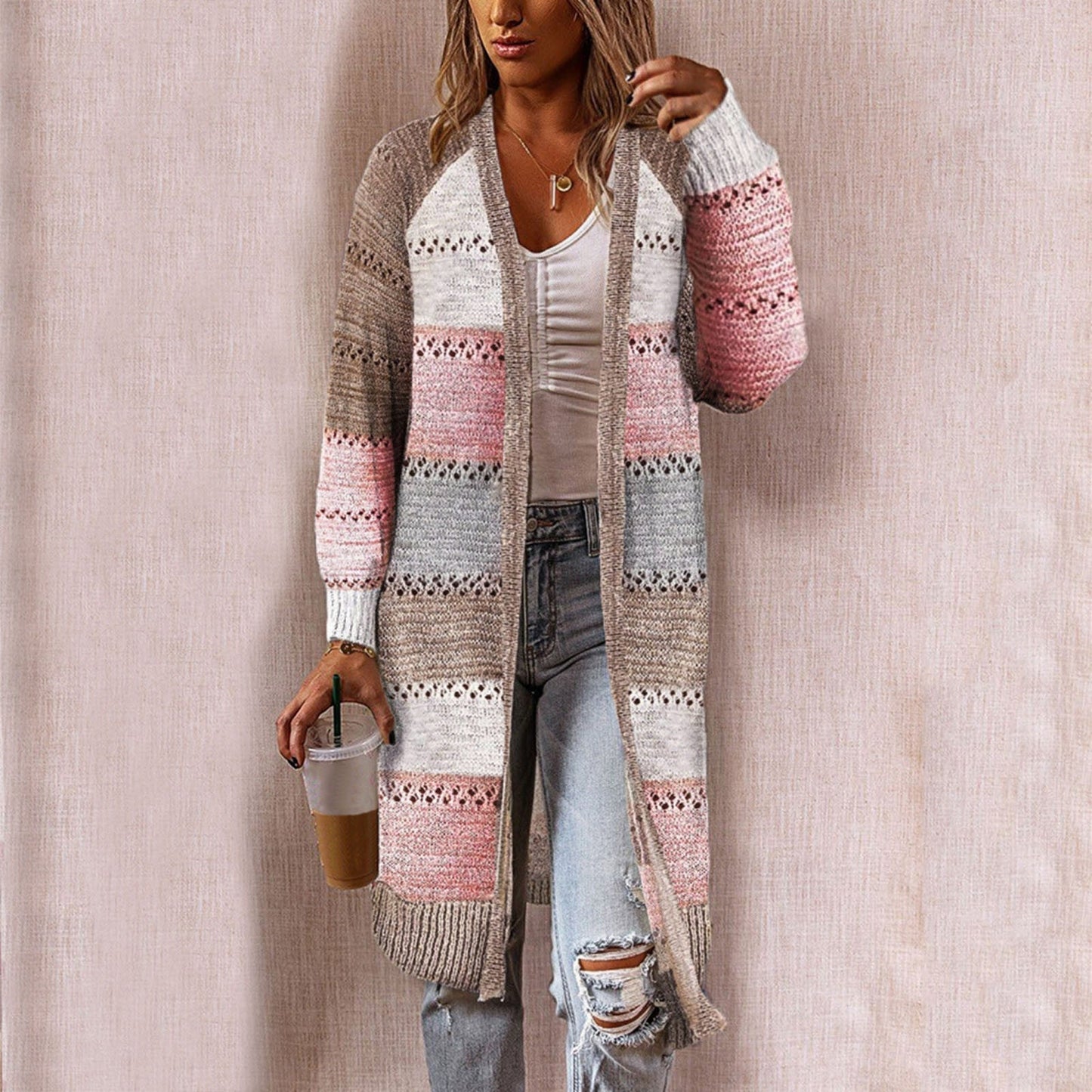 Frau trägt gestreiften Strick-Cardigan in Beige, Rosa und Grau, kombiniert mit zerrissenen Jeans.