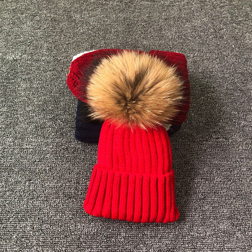 Rote Strickmütze mit Kunstfellbommel auf grauem Teppich, Wintermode Accessoire.