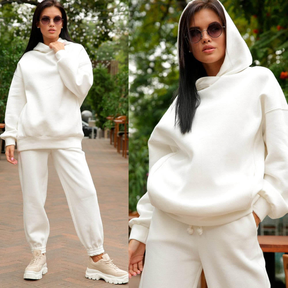 Frau in weißem Hoodie und Jogginghose, Sonnenbrille, lässiger Look, Outdoor-Hintergrund.