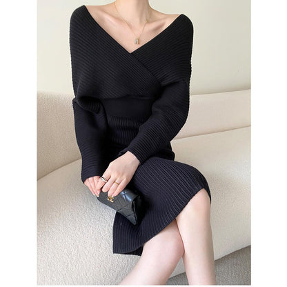 Frau in schwarzem Strickkleid, sitzt auf Sofa, hält schwarze Clutch, elegantes Outfit.