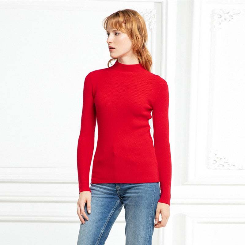 Frau in rotem Rollkragenpullover und blauer Jeans vor weißem Hintergrund.