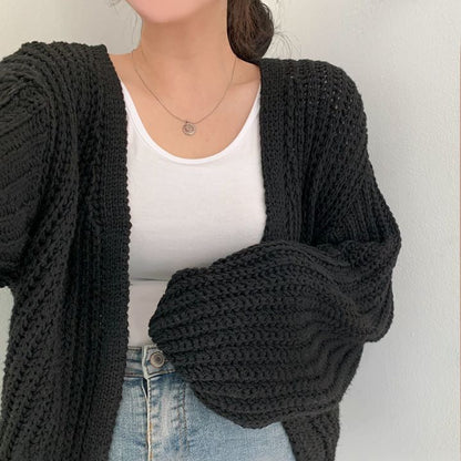 Frau trägt schwarzen Strickcardigan, weißes Top, blaue Jeans; modischer Herbst-Look.