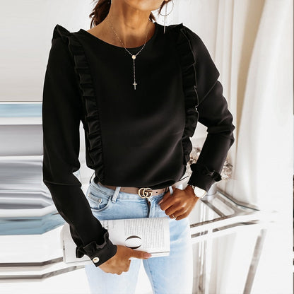Frau in schwarzer Rüschenbluse, Jeans, mit Kreuzkette und Gürtel, hält ein Buch.