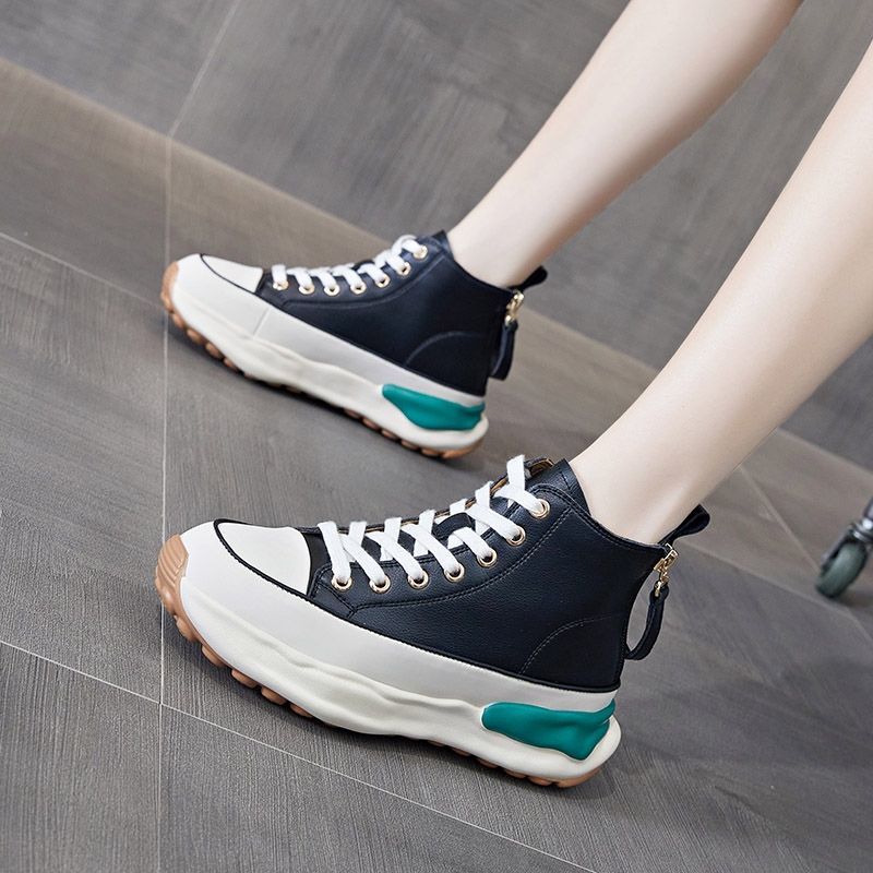 Schwarze High-Top-Sneaker mit weißer Sohle und grünen Akzenten auf grauem Boden.