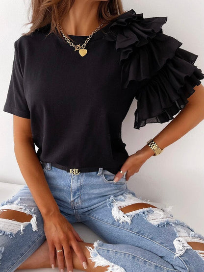 Frau in schwarzem Rüschen-Top und zerrissenen Jeans, modisches Outfit, Goldkette, Armbanduhr.