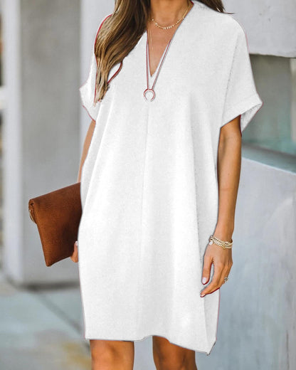 Frau in weißem Sommerkleid mit V-Ausschnitt, braune Clutch, lässiger Stil, Straßenhintergrund.