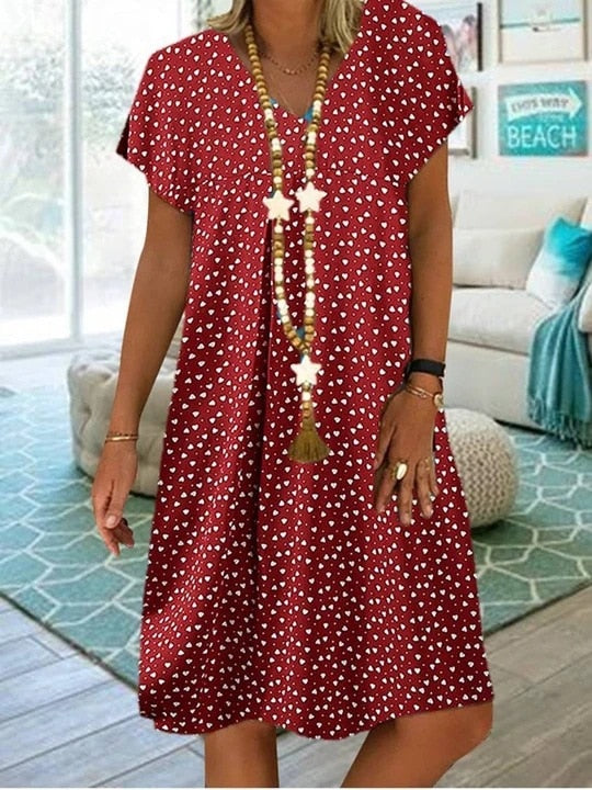 Frau in rotem Sommerkleid mit weißen Punkten und langer Halskette in modernem Wohnzimmer.
